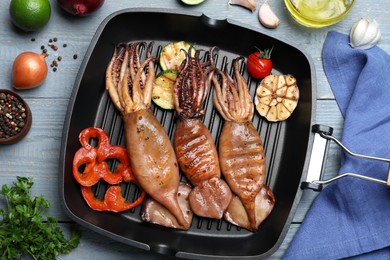 Tasty grilled squids with vegetables served on grey wooden table, flat lay