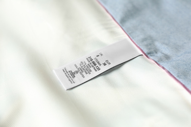 Clothing label with size and content information on light garment, closeup