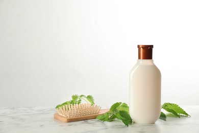 Stinging nettle, cosmetic product and brush on white marble background, space for text. Natural hair care