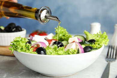 Dressing tasty fresh Greek salad with olive oil on grey marble table