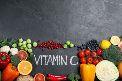 Phrase VITAMIN C and different products on black table, flat lay. Space for text
