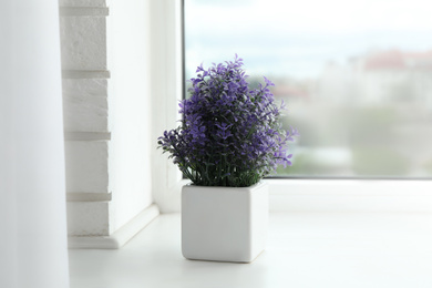 Beautiful artificial plant in flower pot on window sill
