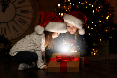 Cute children opening magic gift box near Christmas tree at night