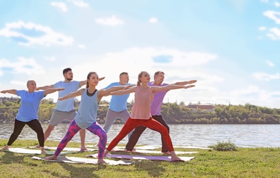 Group of people practicing yoga near river on sunny day