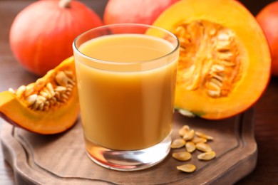 Photo of Tasty pumpkin juice in glass, whole and cut pumpkins on wooden table, closeup