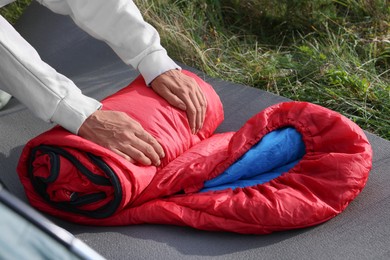Woman folding red sleeping bag outdoors, closeup