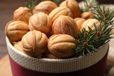 Photo of Bowl of delicious nut shaped cookies and fir tree branches on wooden table, closeup