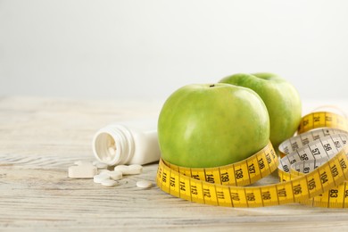 Jar of weight loss pills, apples and measuring tape on white wooden table
