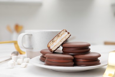 Saucer with delicious choco pies and cup of drink on white table indoors, closeup