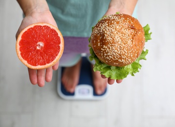 Choice concept. Top view of woman with grapefruit and burger standing on scales, closeup