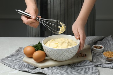 Photo of Woman making homemade mayonnaise in ceramic bowl at light grey marble table, closeup