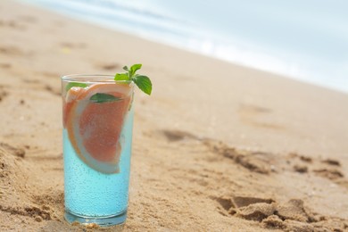 Glass of refreshing drink with grapefruit and mint on sandy beach near sea, space for text