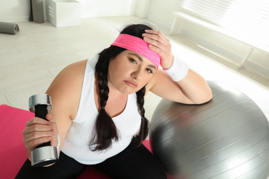Lazy overweight woman with fit ball and dumbbell at gym