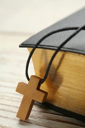 Christian cross and Bible on white wooden table, closeup