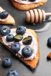 Tasty sandwiches with cream cheese, honey and berries on grey table, closeup