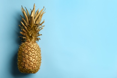 Photo of Top view of painted golden pineapple on light blue background, space for text. Creative concept
