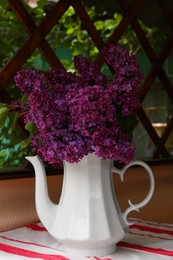 Beautiful lilac flowers in teapot near window indoors