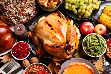 Traditional Thanksgiving day feast with delicious cooked turkey and other seasonal dishes served on black wooden table, flat lay