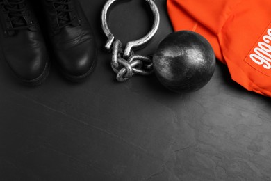Prisoner ball with chain, jail clothes and boots on black table, flat lay. Space for text