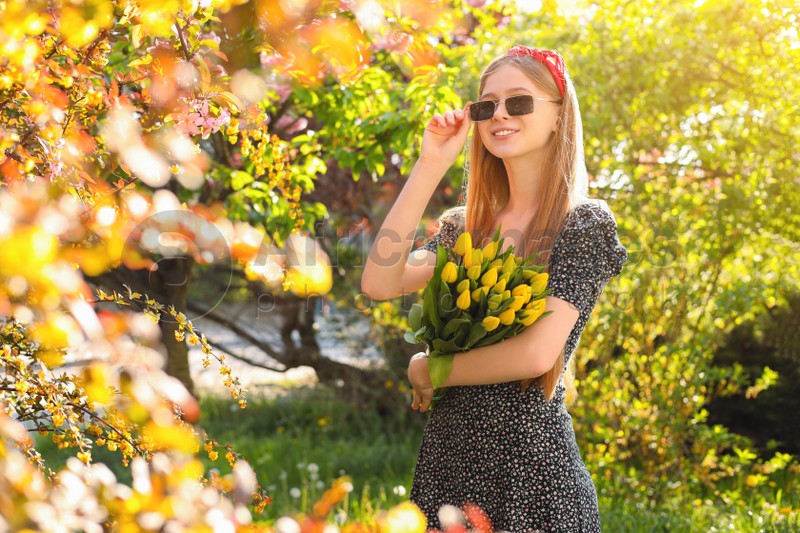 Beautiful teenage girl with bouquet of yellow tulips in park on sunny day