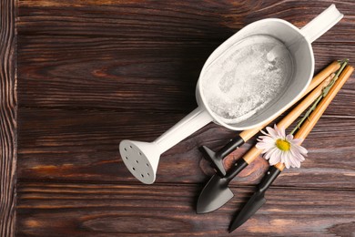 Photo of Watering can with gardening tools and flower on wooden table, top view
