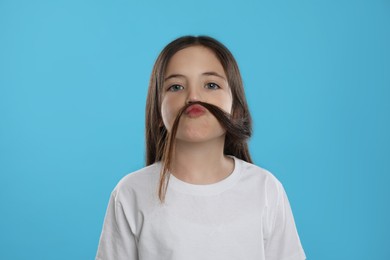 Photo of Cute little girl making fake mustache with her hair on turquoise background
