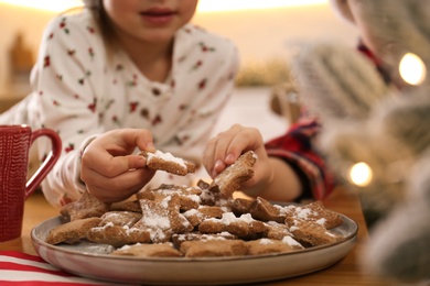 Little children taking tasty Christmas cookies from plate at table, closeup