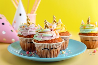 Photo of Cute sweet unicorn cupcakes and party items on yellow background