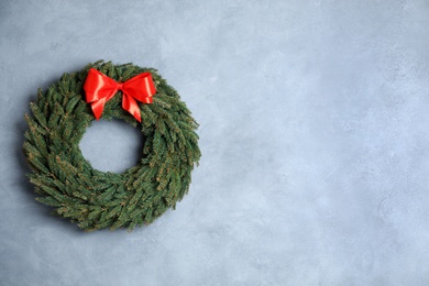 Christmas wreath made of fir branches with red bow on color wall. Space for text