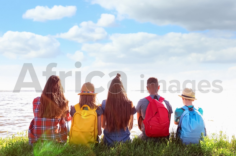 School holidays. Group of children sitting on green grass near river 