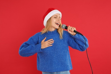Happy woman in Santa Claus hat singing with microphone on red background. Christmas music