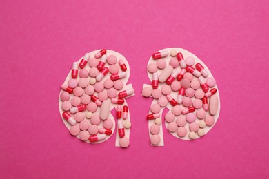 Paper cutout of kidneys with pills on magenta background, top view