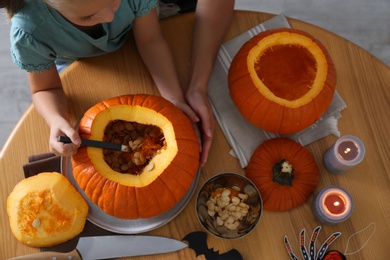 Mother and daughter making pumpkin jack o'lantern at wooden table, top view. Halloween celebration