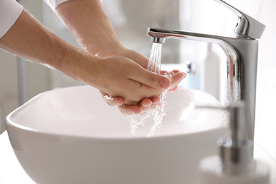 Man washing hands over sink in bathroom, closeup