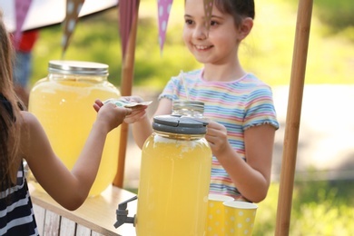 Little girl selling natural lemonade to kid in park. Summer refreshing drink