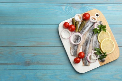Photo of Serving board with salted herring fillets, parsley, onion rings, pickles, cherry tomatoes and lemon on light blue wooden table, top view. Space for text