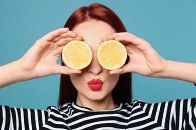 Photo of Redhead woman covering eyes with lemons and blowing kiss on light blue background