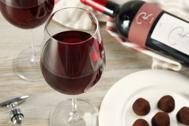 Glass of red wine with chocolate candies on white wooden table, closeup