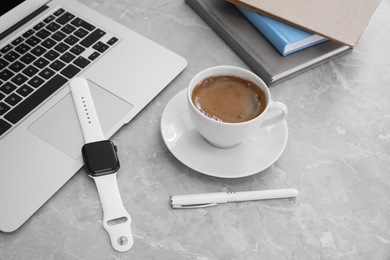 Stylish smart watch, laptop and cup of coffee on grey marble table