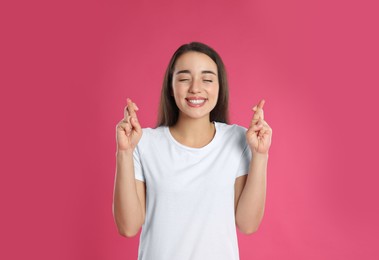 Woman with crossed fingers on pink background. Superstition concept