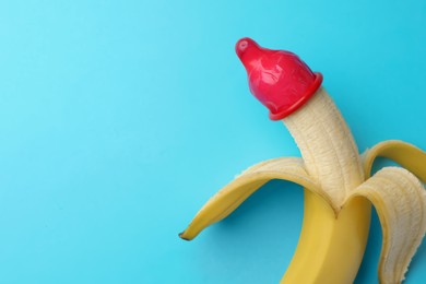 Banana with condom on light blue background, top view and space for text. Safe sex concept