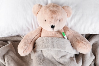 Toy bear with thermometer lying in bed, top view. Children's hospital