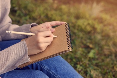 Young woman drawing with pencil in sketchbook outdoors, closeup