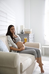 Young pregnant woman with glass of juice in living room. Taking care of baby health
