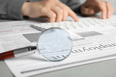 Looking through magnifying glass at newspaper and woman on background, closeup. Job search concept
