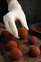 Photo of Confectioner preparing delicious chocolate truffles powdered with cocoa at table, closeup