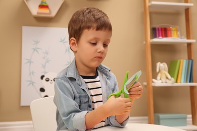 Photo of Little boy cutting color paper with scissors at table indoors