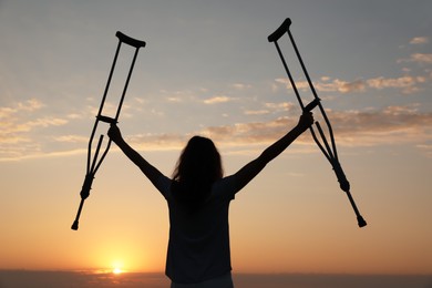 Woman holding axillary crutches outdoors at sunrise, back view. Healing miracle
