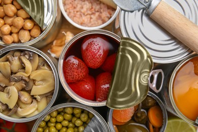 Photo of Open tin cans with different preserved products on wooden board, flat lay