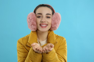 Beautiful young woman wearing earmuffs on light blue background
